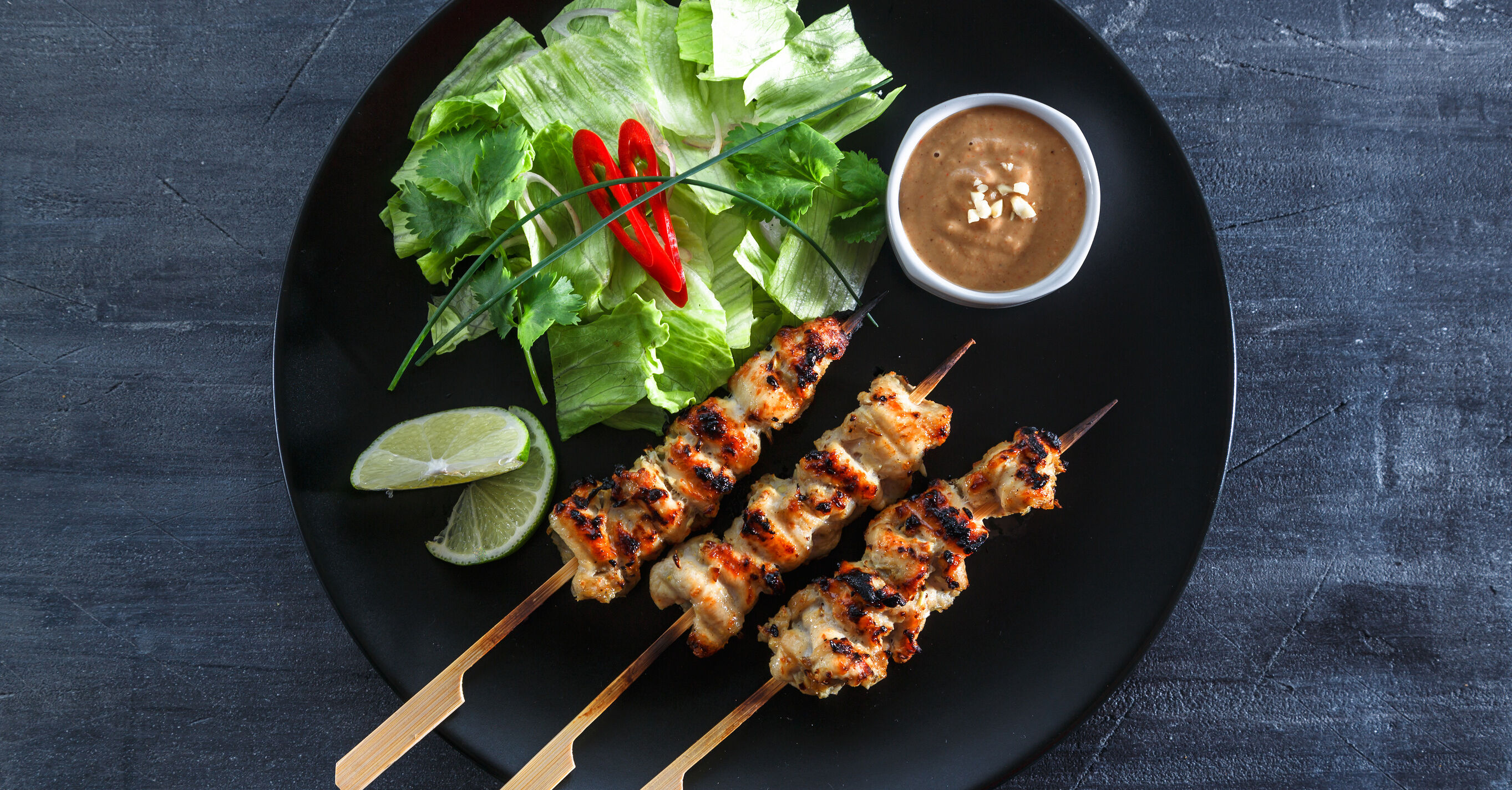 Chicken Satay on a plate with a salad, lime and peanut sauce