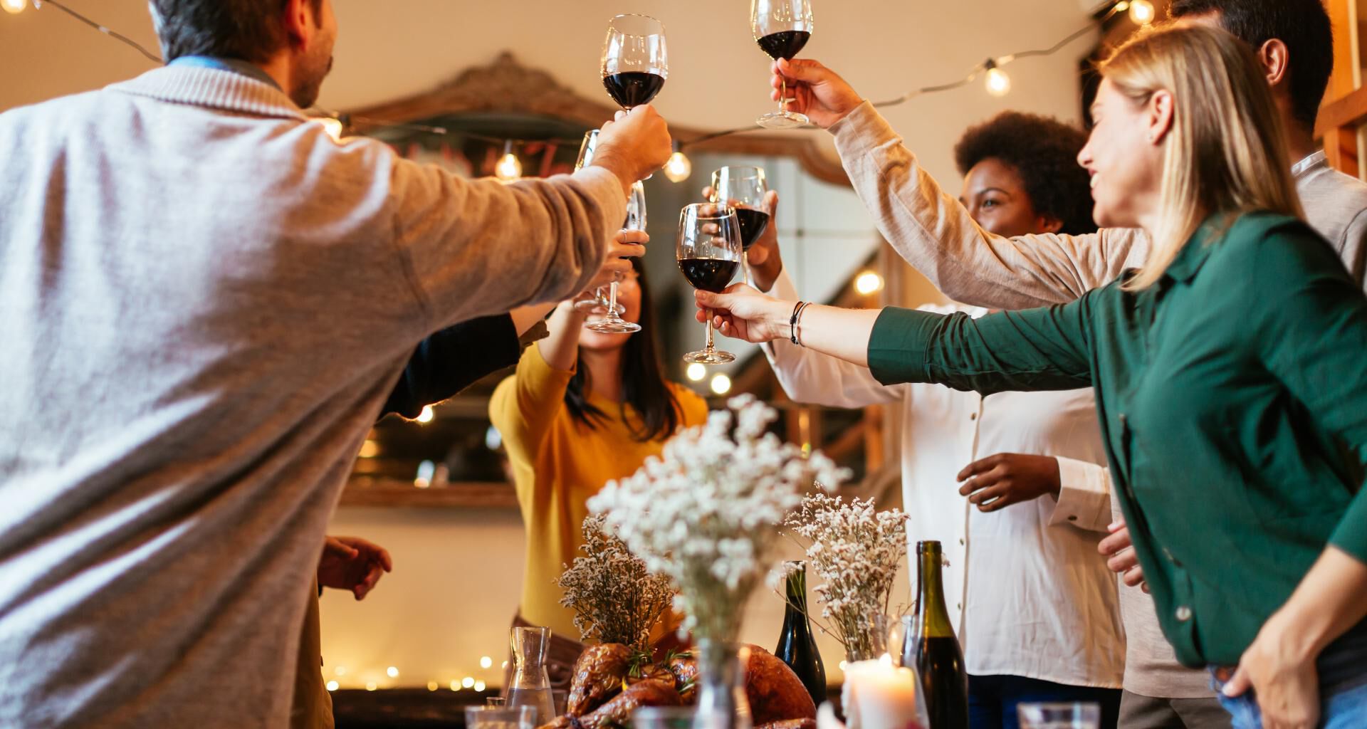 People saying cheers with glasses of red wine over dinner table.