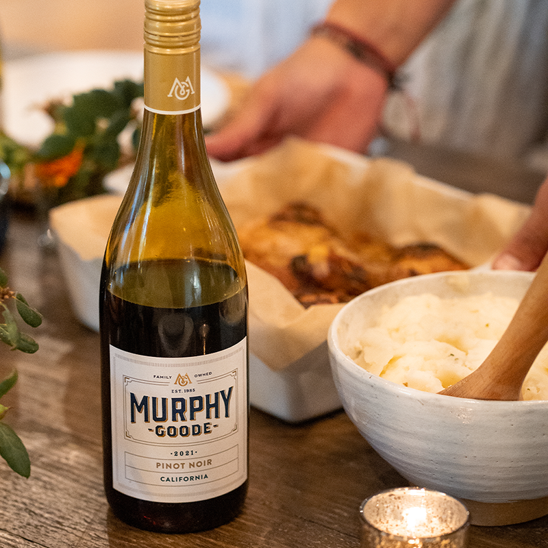 A table with plates of food, glasses of water, and open bottles of Murphy Goode Sauvignon blanc and Pinot Noir.