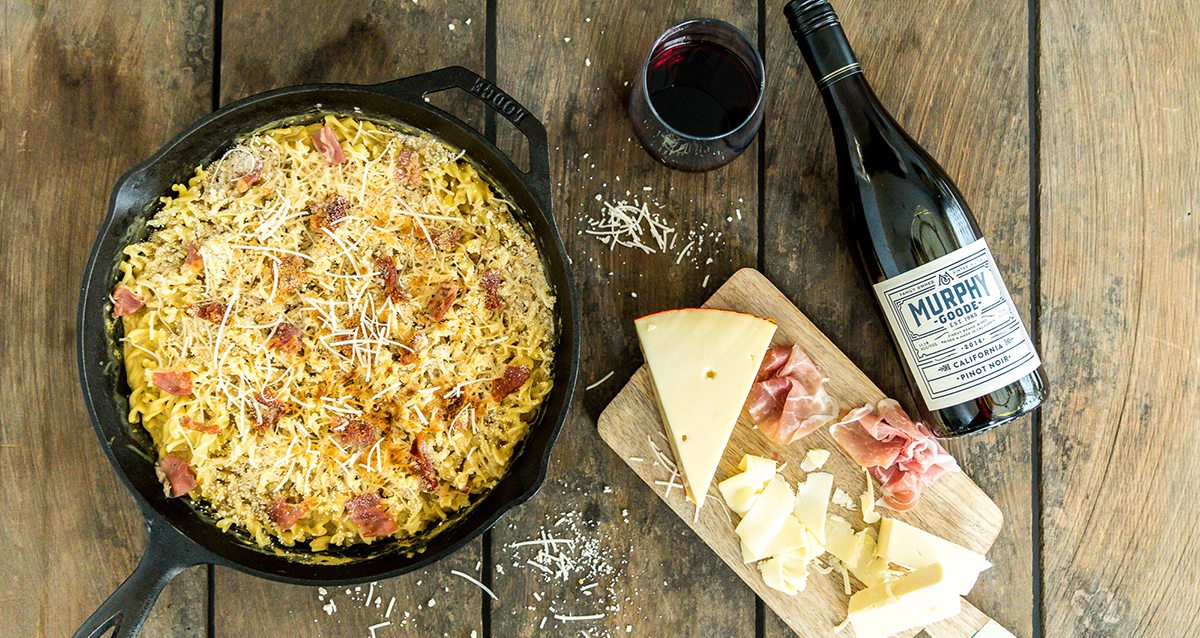 Cast iron macaroni and cheese with a block of cheese and a bottle of Murphy-Goode Wine