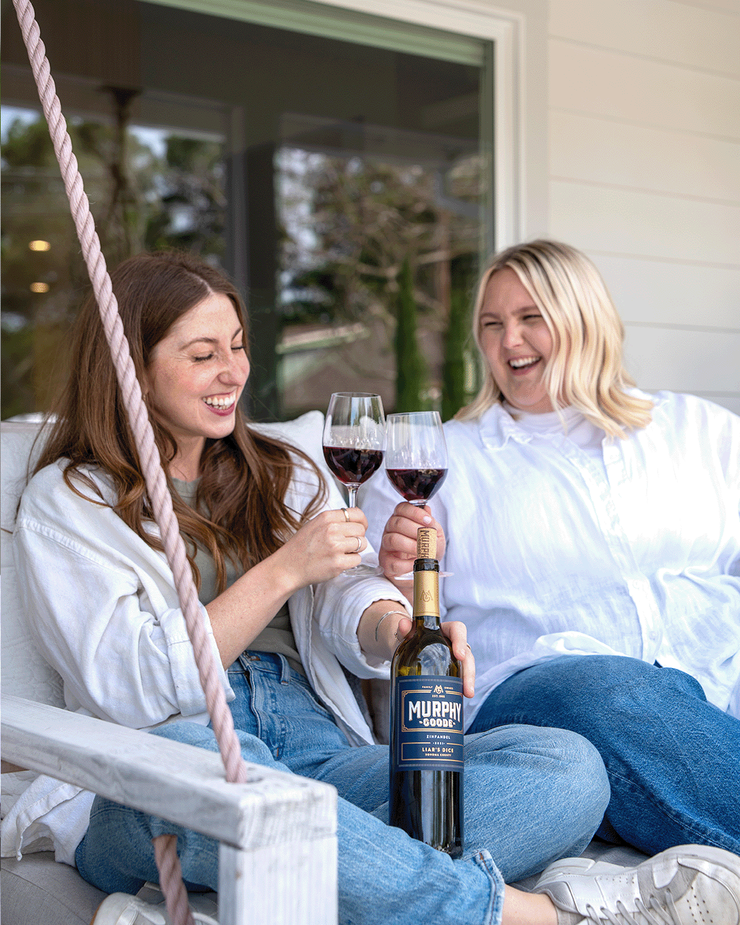 two female friends enjoying glasses of red wine on their front porch